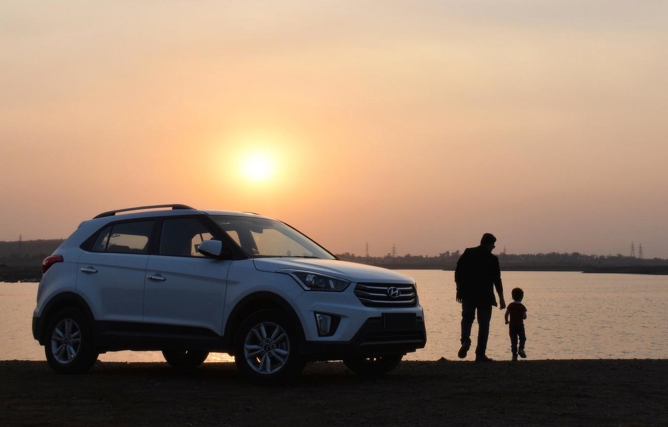 White Hyundai car with the onset in the horizon and father and son holding hands.