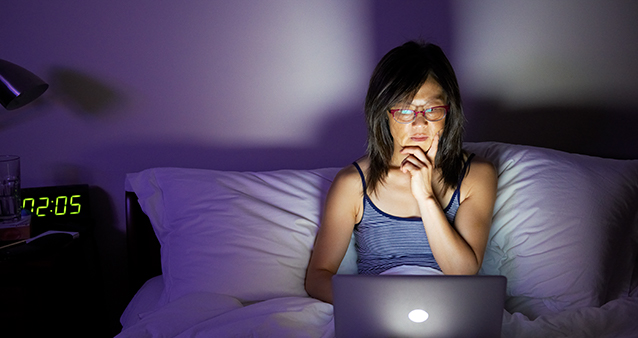 Woman in bed working on a laptop, rather than getting adequate sleep to cope with COVID-19