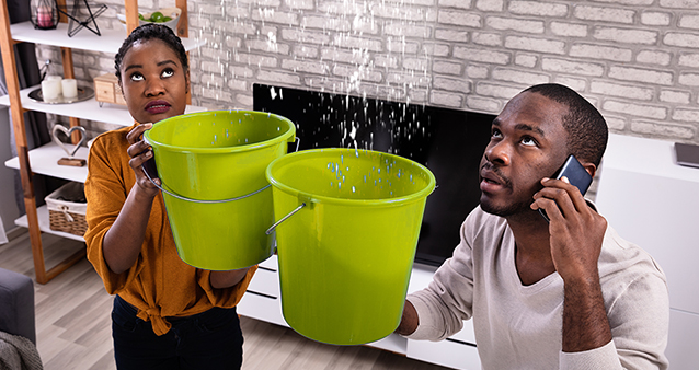 Young couple standing with buckets to catch water leaking from their ceiling
