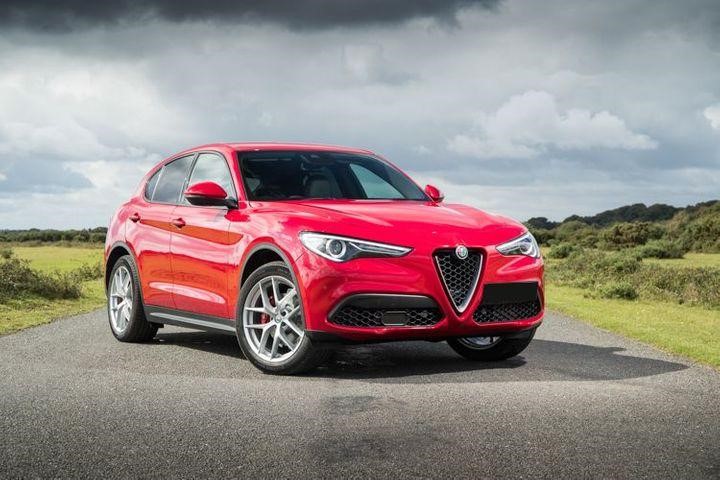 Red Alfa Romeo stelvio parked sideways on tar road with green on sides.