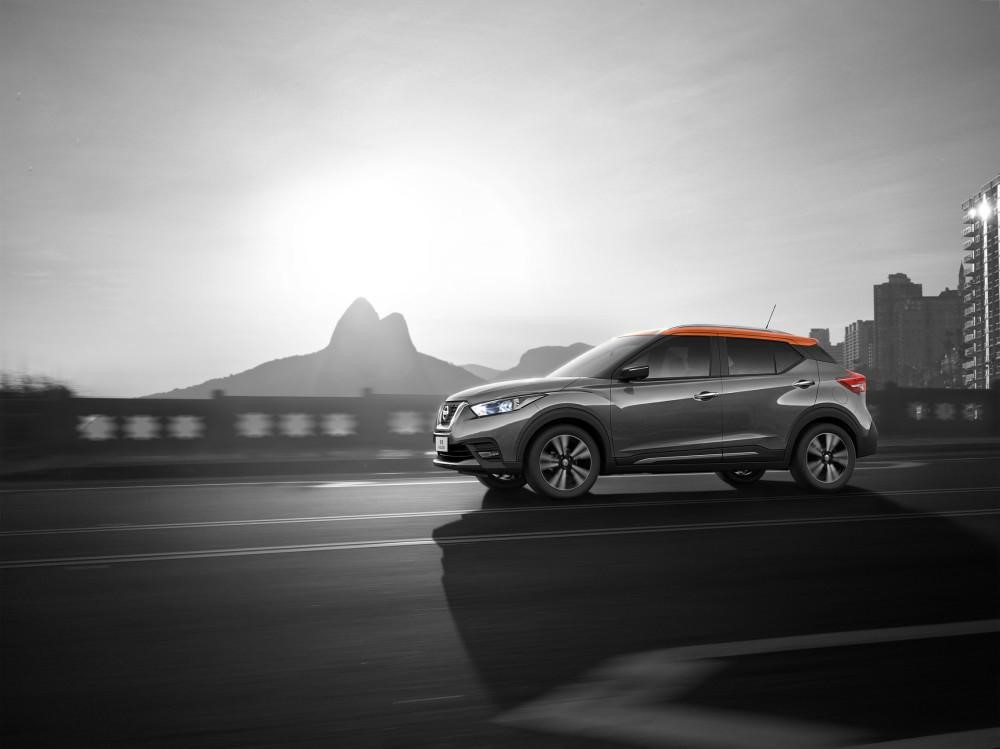 Grey Nissan kicks, driving, side view with mountain and buildings in the background.