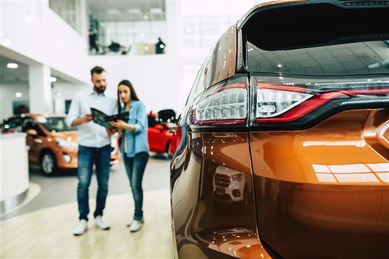 Couple stands in a car showroom looking at the details of a new car 