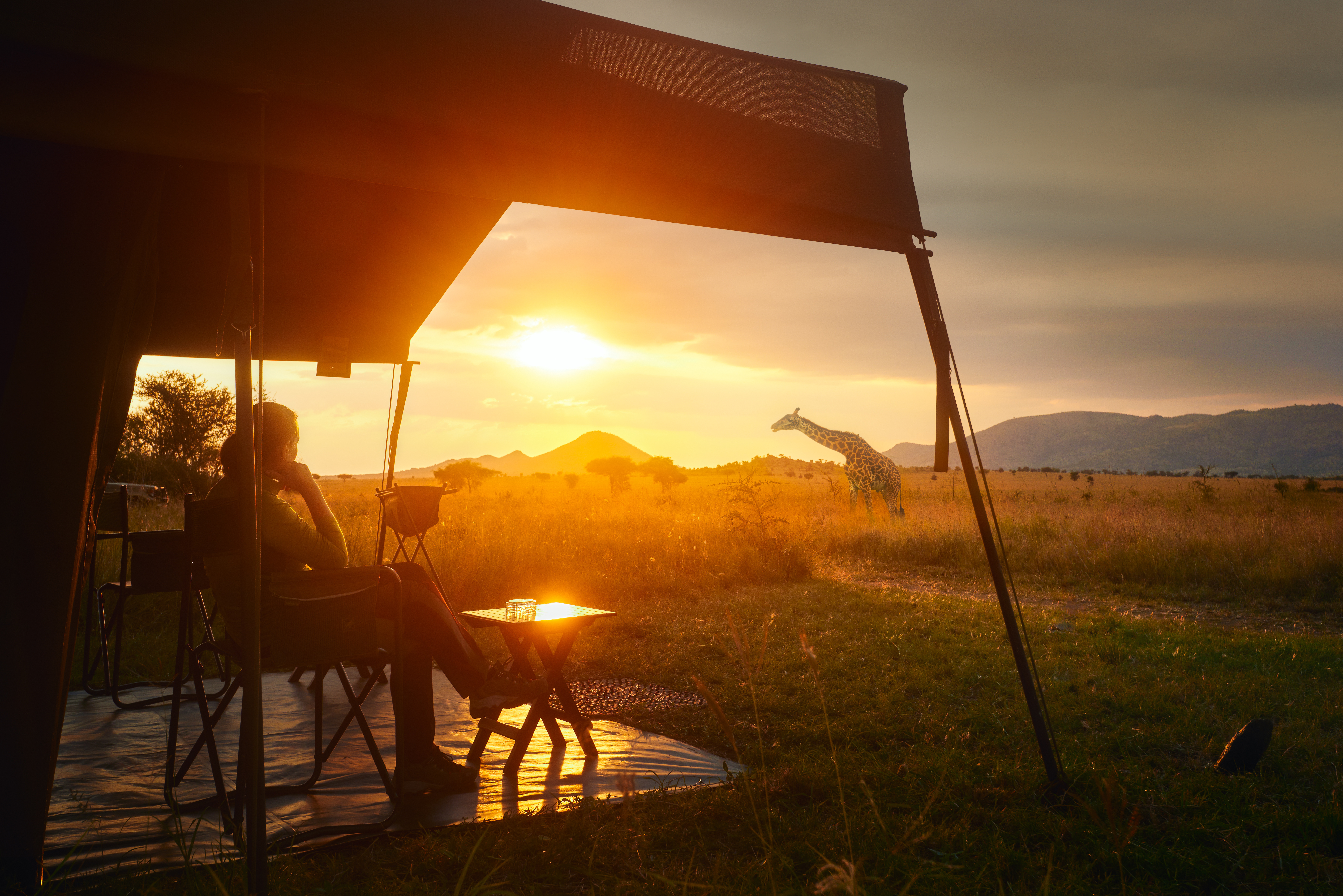 Silhouette of a person relaxing under a camping awning at sunset