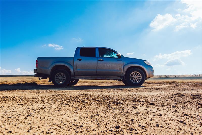 Silver pickup truck driving on a dirt road under a clear blue sky.