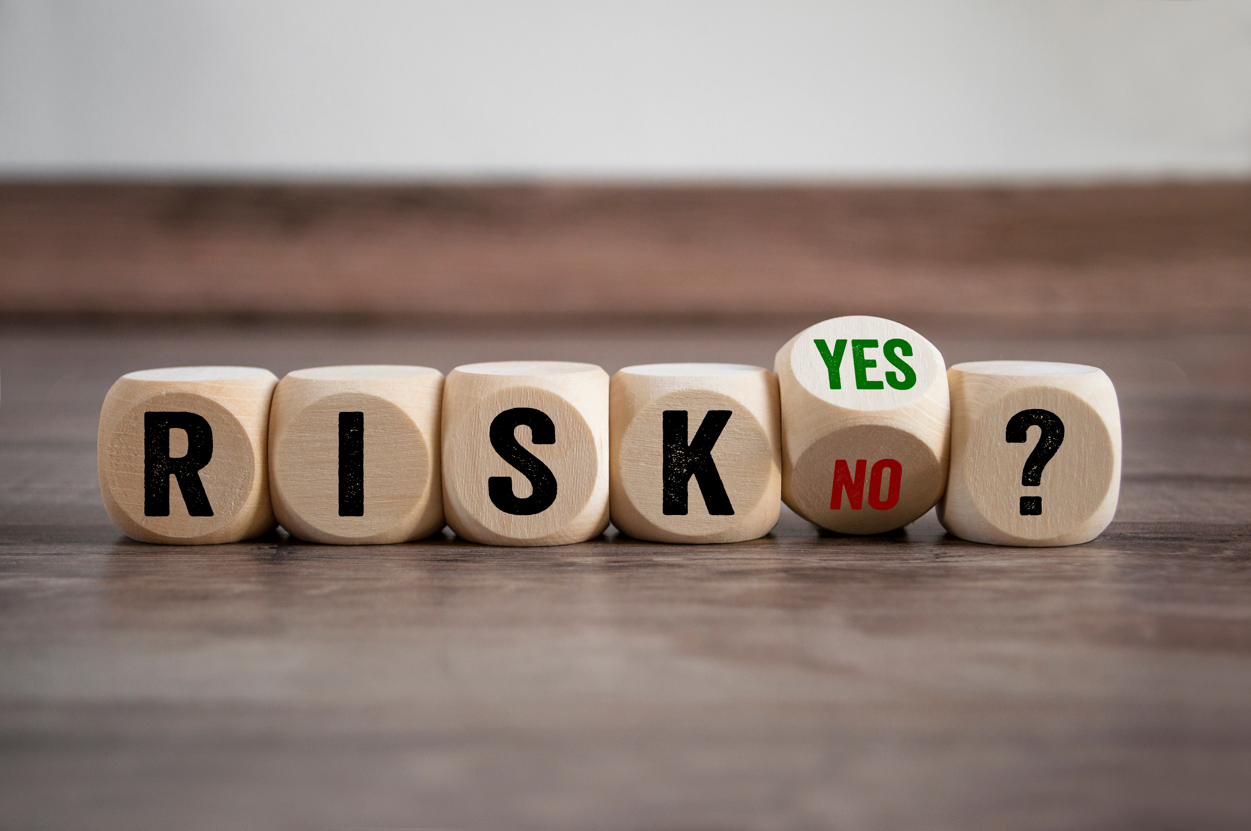 Wooden blocks spelling out the word ‘RISK’ alongside blocks labeled ‘YES,’ ‘NO,’ and a question mark.