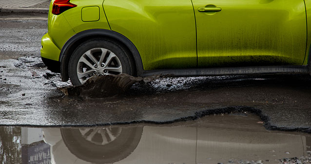 green car driving through a large pothole