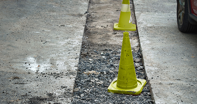 traffic cones in a large pothole in the middle of a road