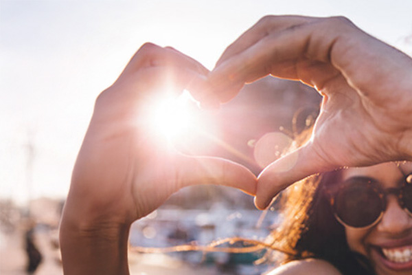 Lady with hands in shape of heart with sun shining in background